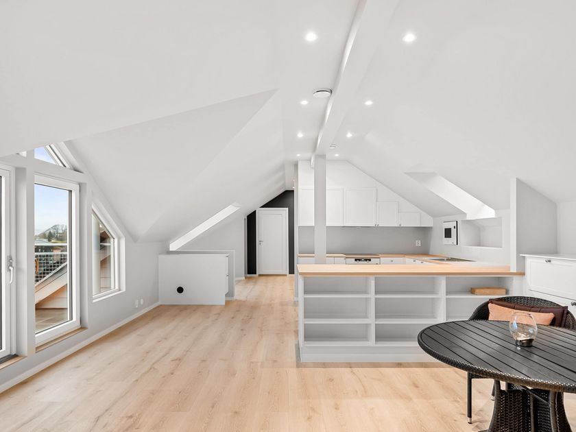 Loft bygget om til ett stort rom med skråtak, synlig ås og utgang til balkong