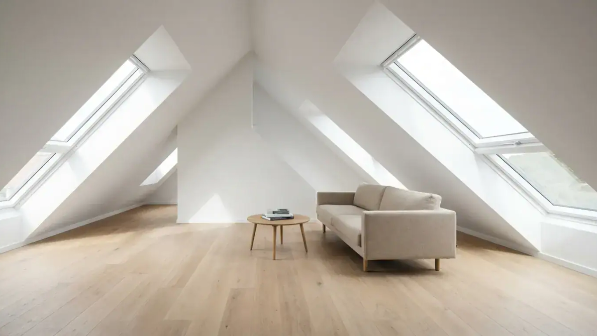 Et lyst og nyoppusset loft med store takvinduer som slipper inn mye dagslys og viser en moderne stueflate
